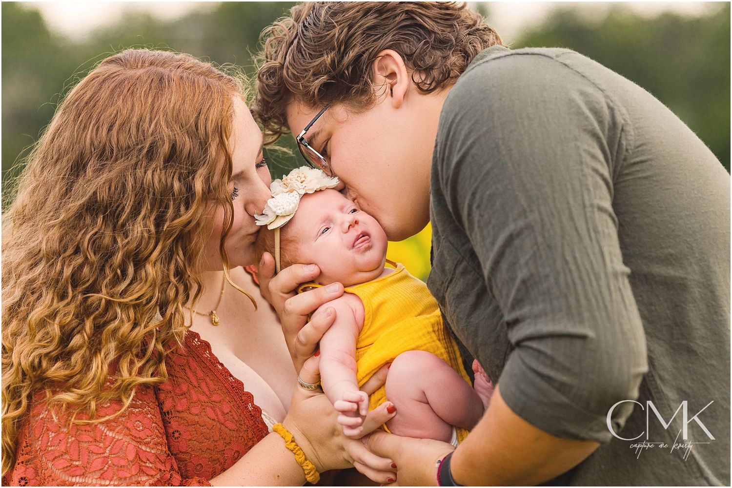 Parents share loving kisses with their baby in yellow during outdoor photo session.