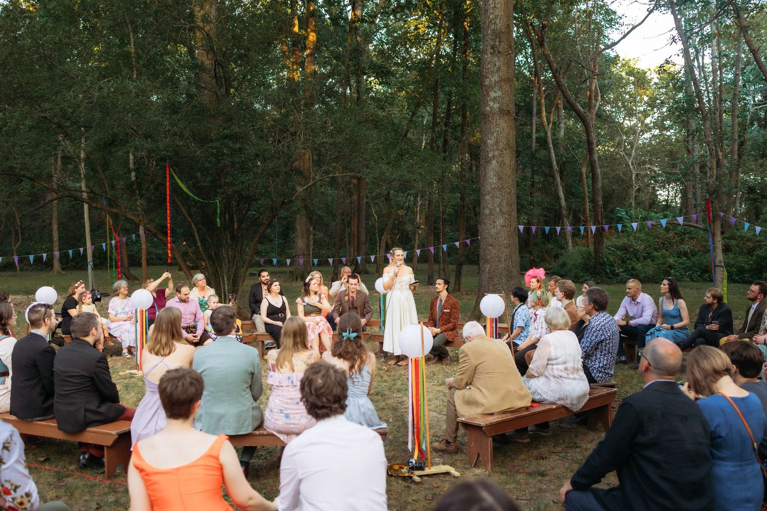 Wedding ceremony audience seated in wooden chairs within forest setting.