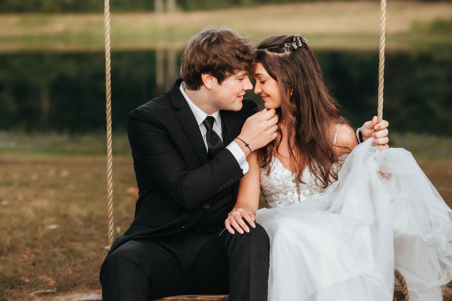 Romantic newlyweds share an intimate moment together on a wooden swing in an outdoor setting.