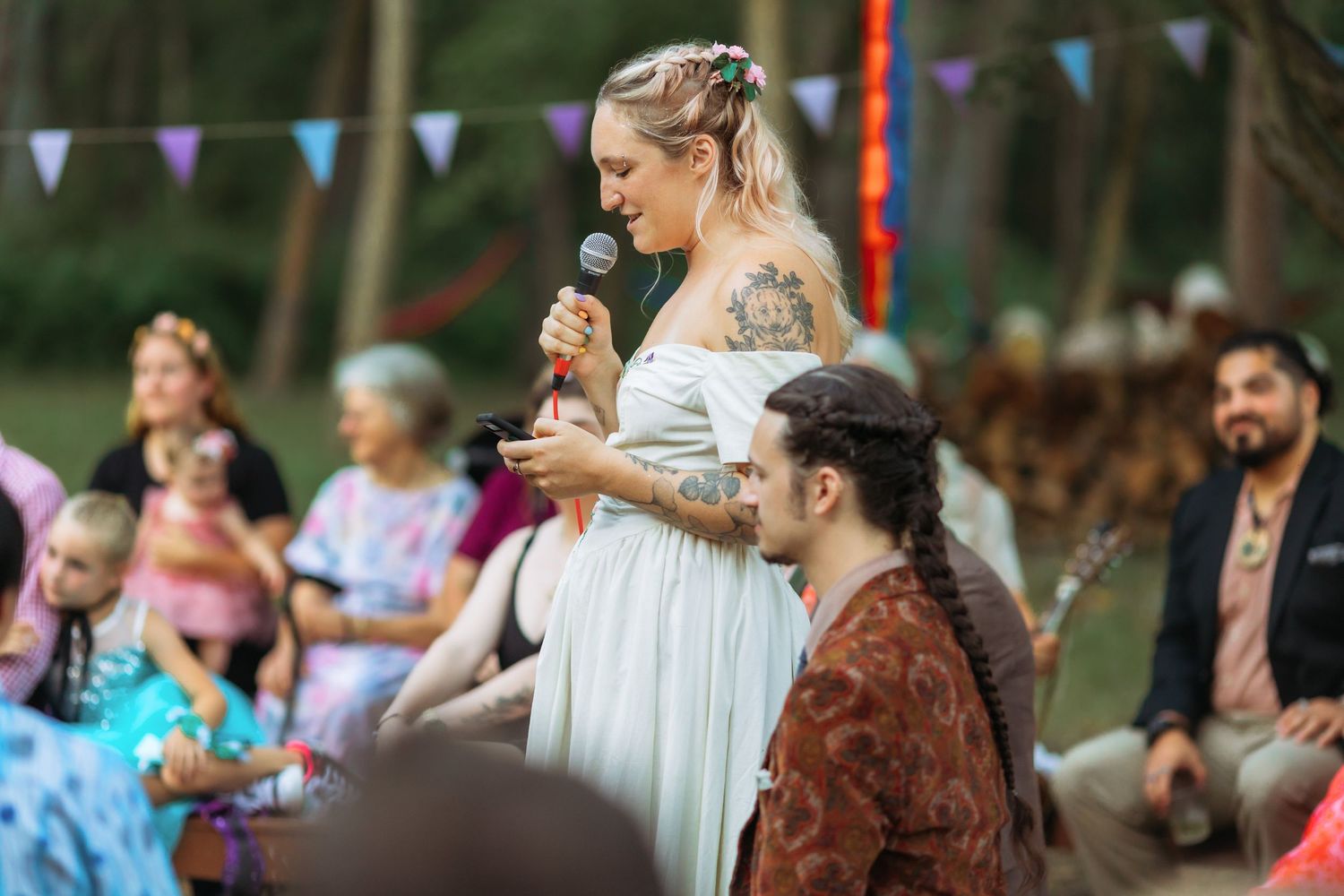 An outdoor wedding reception with guests enjoying speeches under colorful bunting decorations.