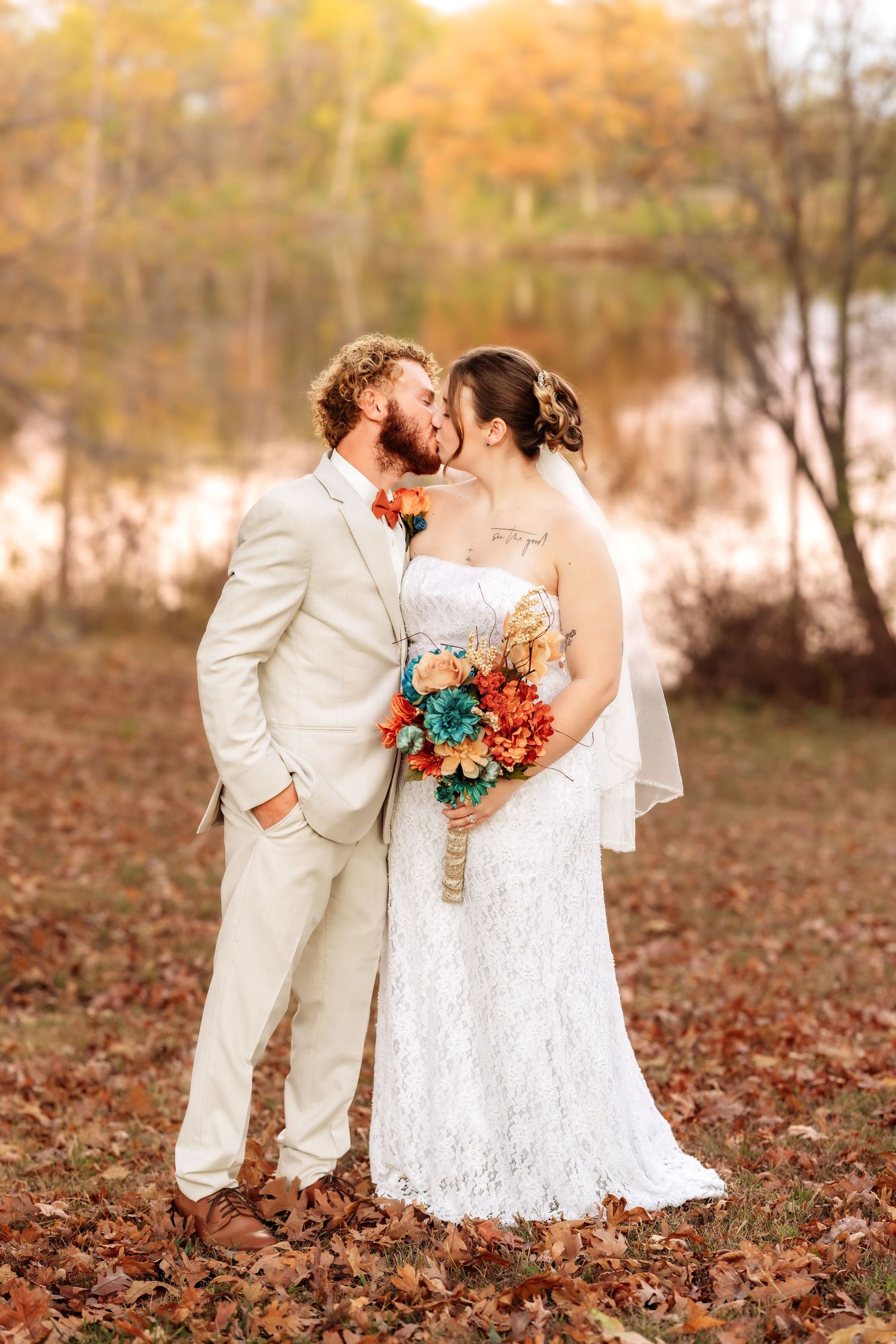 Newlyweds share an intimate moment among fallen autumn leaves in a sunlit outdoor setting.