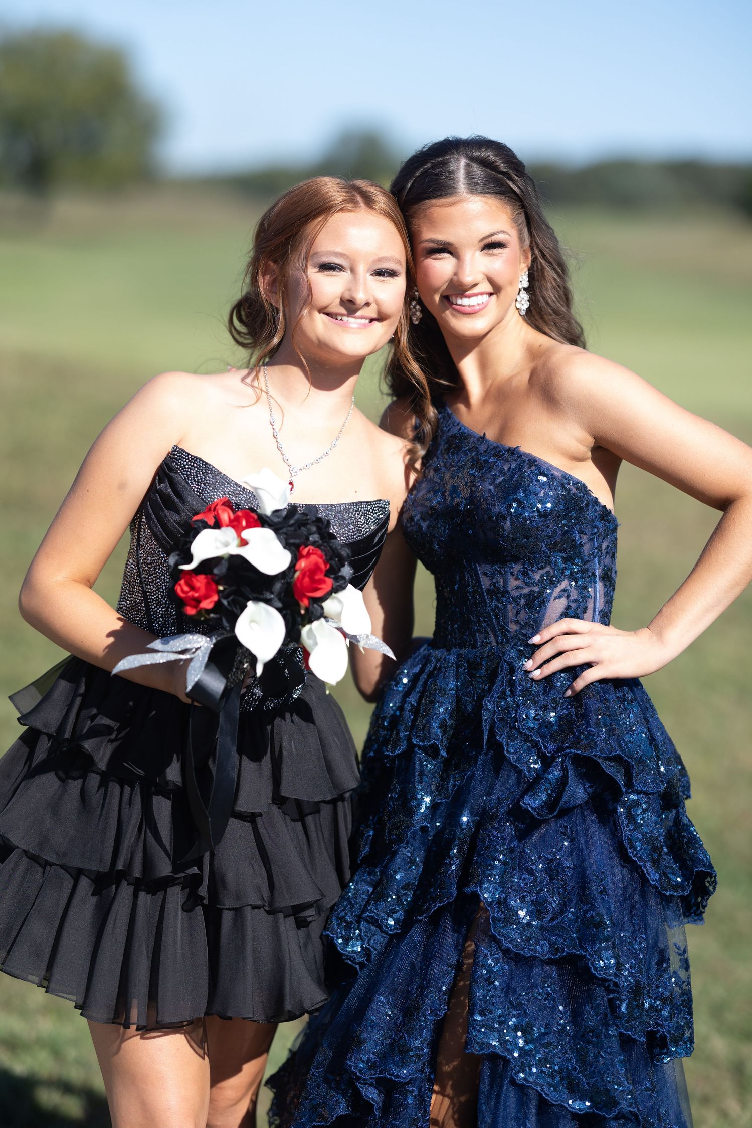 Two friends pose together in formal dresses, one in black and one in navy blue sequins.