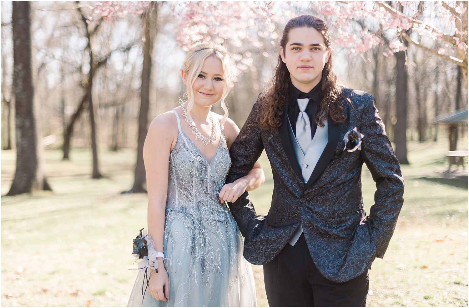 A couple in formal wear pose together under cherry blossom trees.