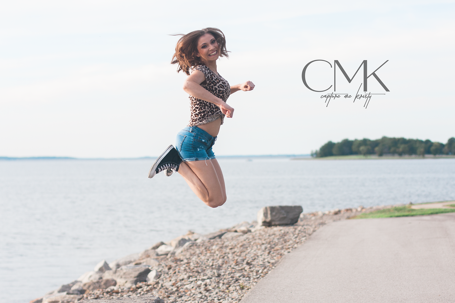 Action shot capturing joyful mid-air jump along waterfront path on sunny day.