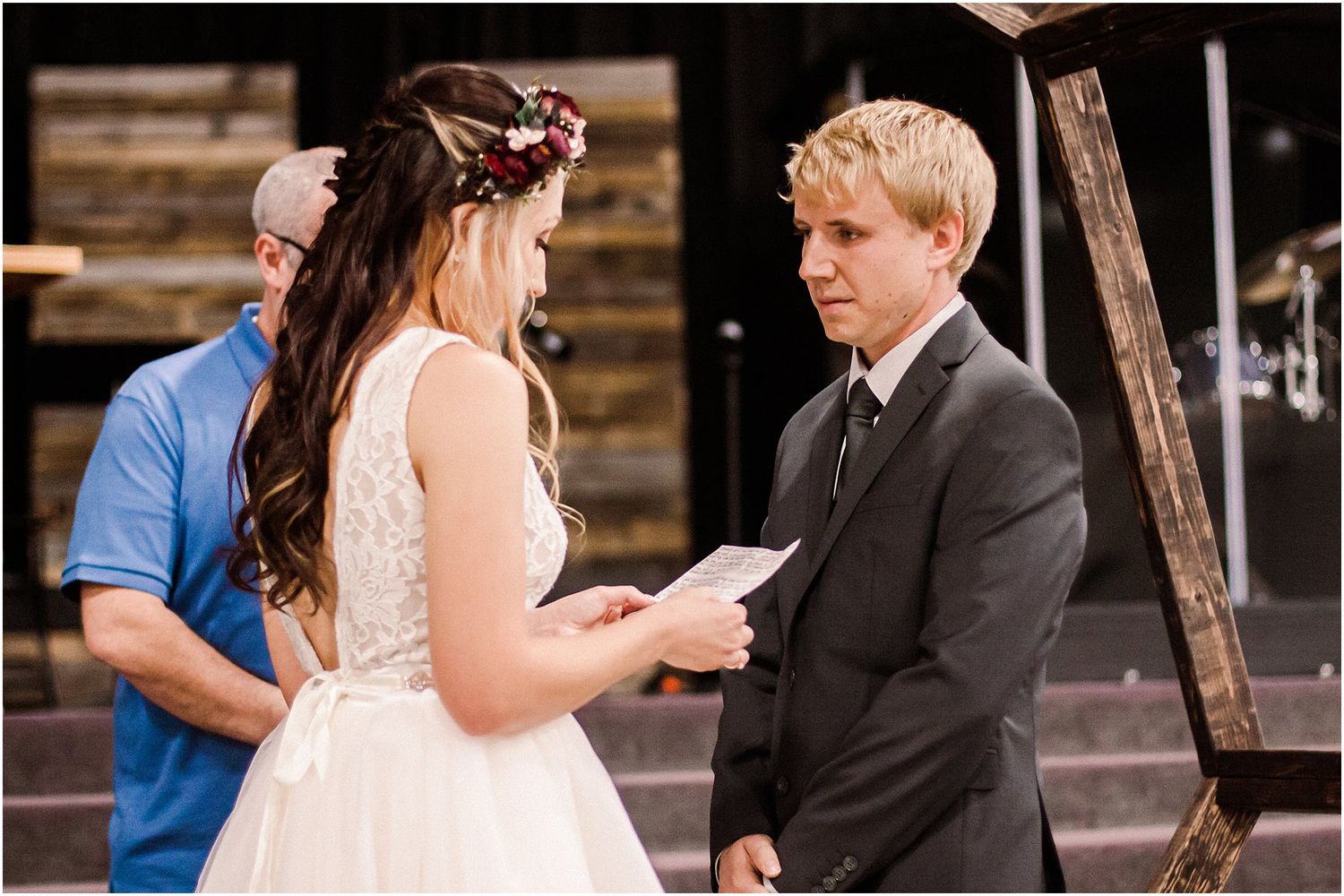 A couple exchanges vows beneath a wooden arch during an intimate wedding ceremony with string lights.