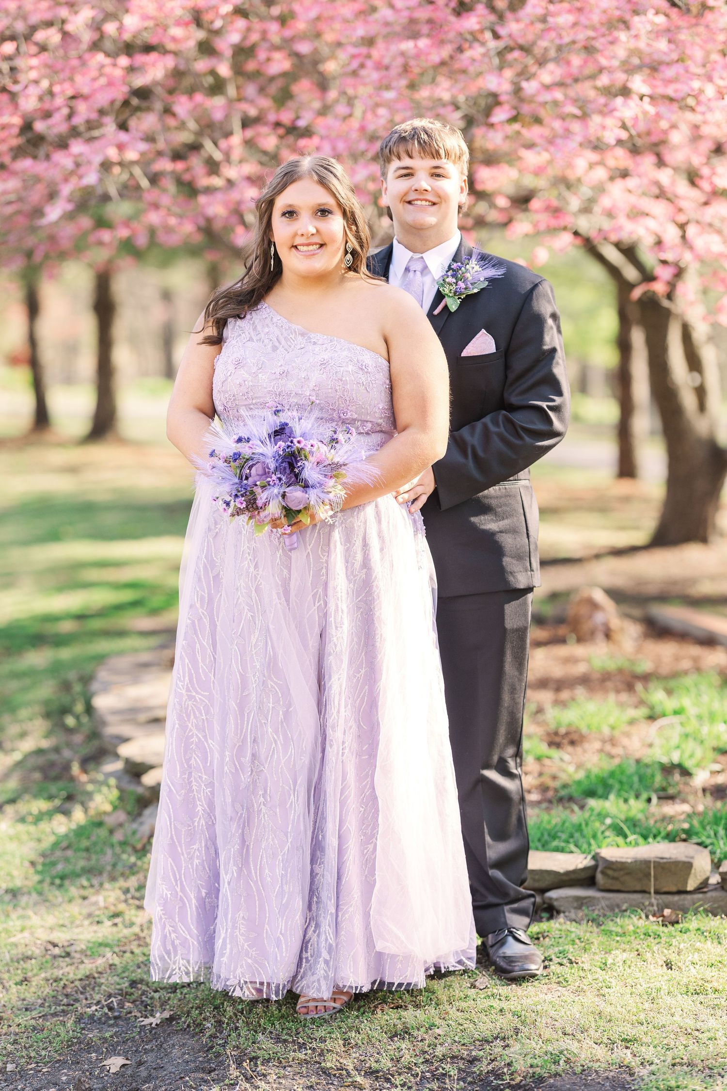 Spring portraits under cherry blossoms with person wearing lavender lace dress.