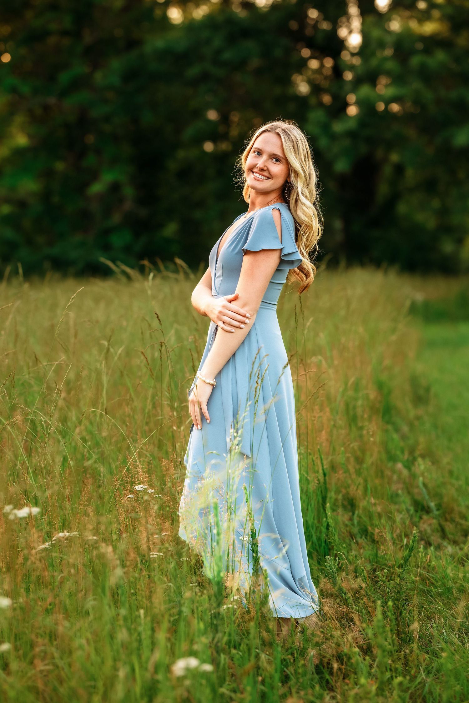 Woman in light blue dress twirling in a summer meadow at sunset.