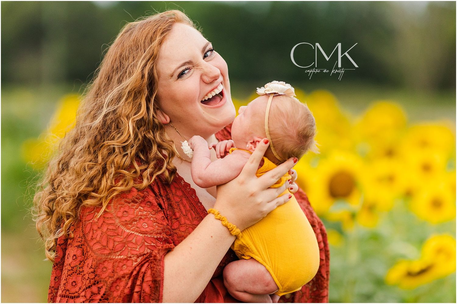Joyful moment between parent and baby in sunflower field wearing rust-colored dress.