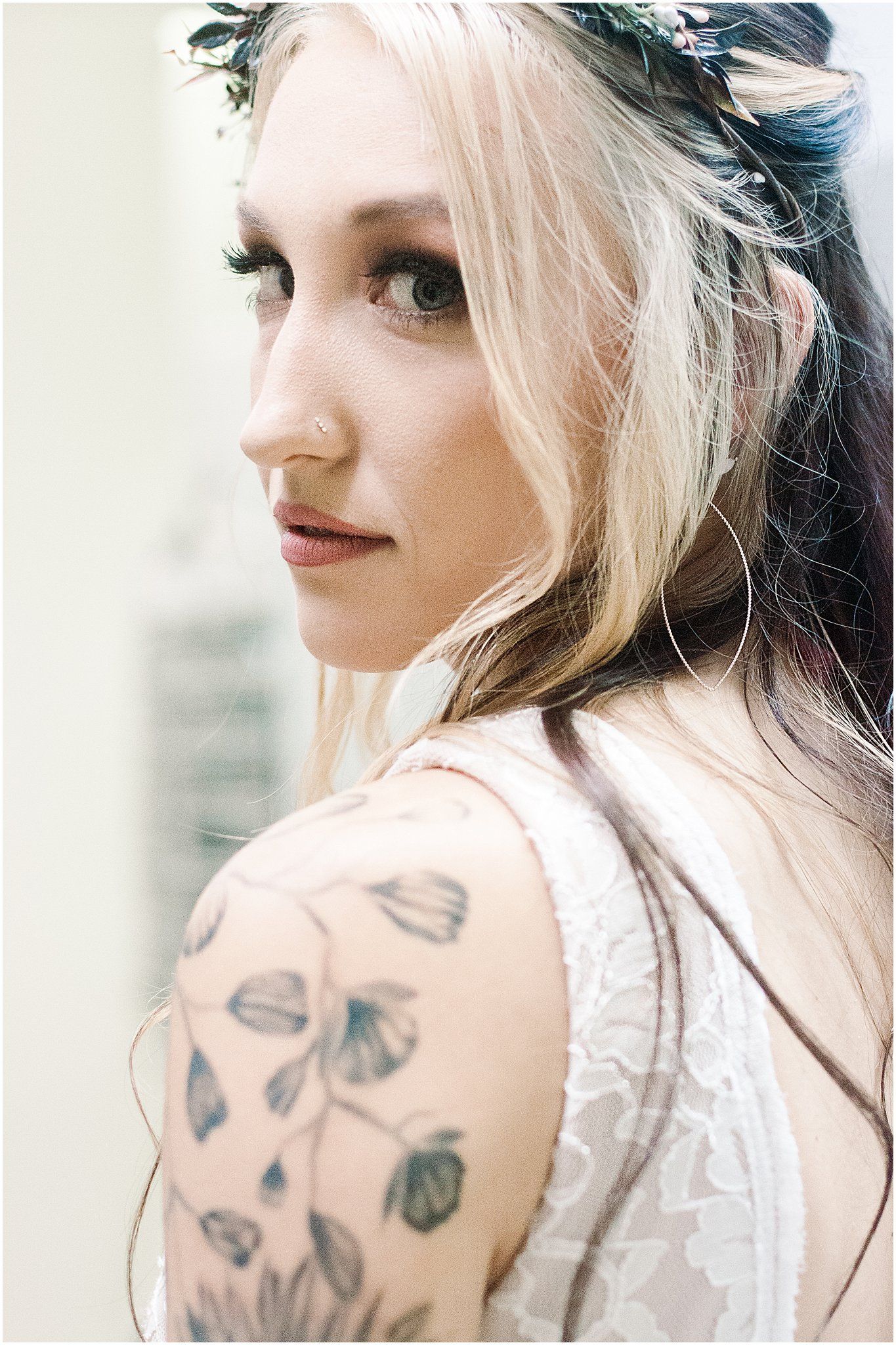 Side profile showing delicate floral crown and botanical arm tattoo against white wedding dress.