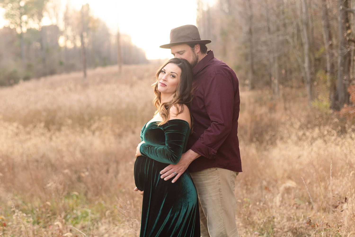 Maternity photo of couple in burgundy and green velvet against autumn foliage.