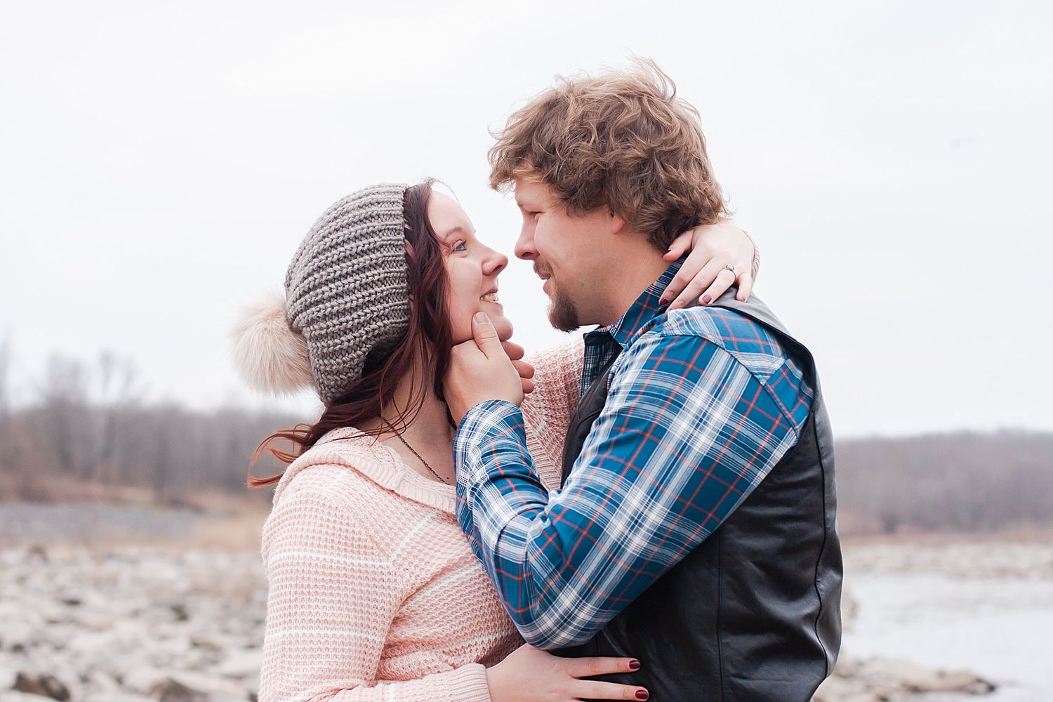 A romantic winter engagement photo showing a couple in knit wear embracing on a cloudy beach.