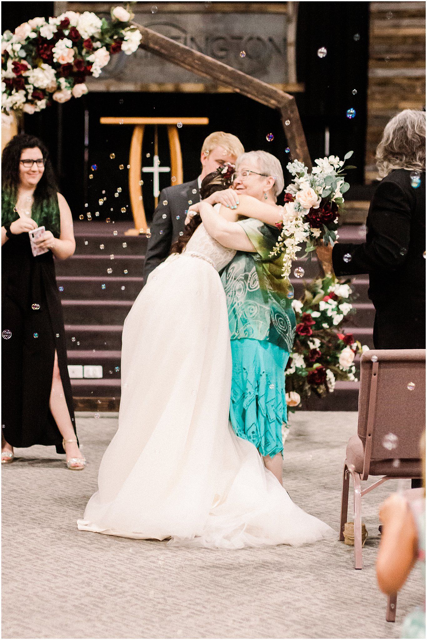 Emotional wedding moment captured near wooden stairs decorated with white and red flowers.