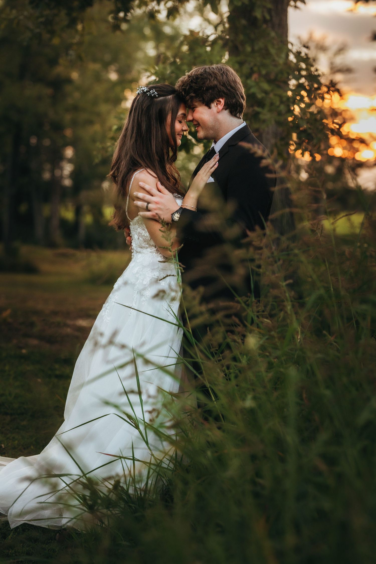 A romantic sunset wedding portrait of a couple embracing in a field with golden light filtering through trees.
