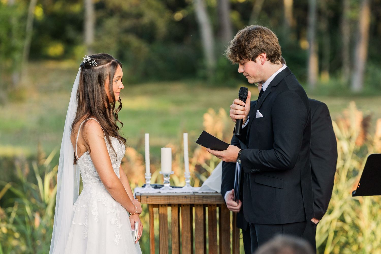 Couple reading personal vows during outdoor ceremony under wooden pergola.