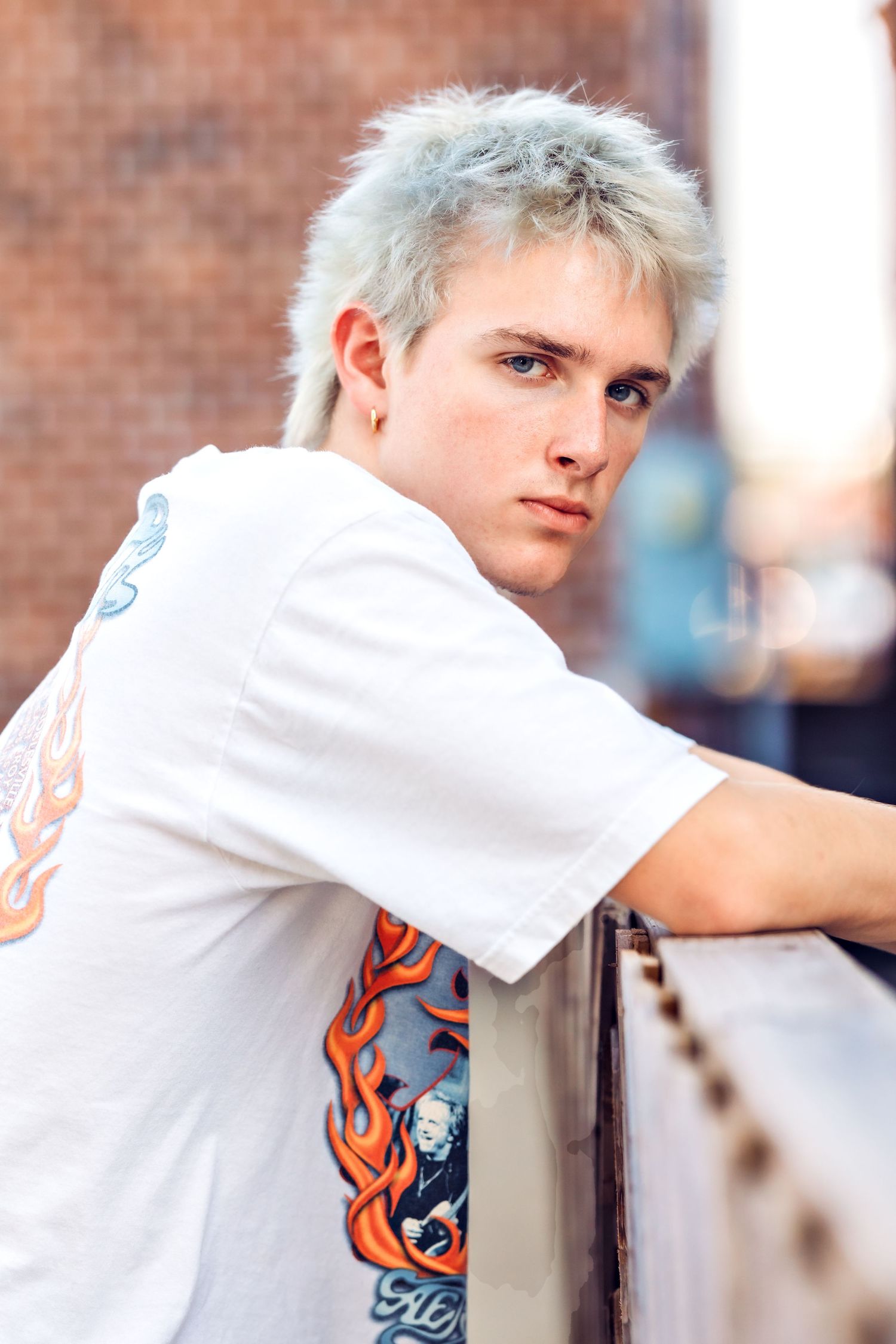 Person wearing white t-shirt with flame design posing against brick wall background.