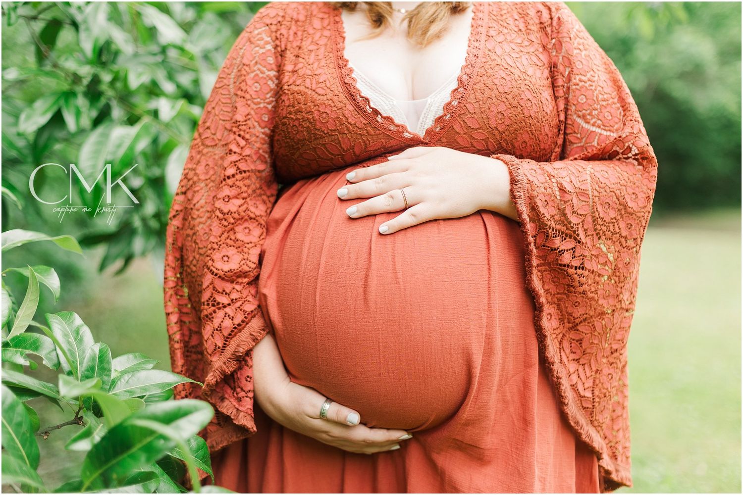 A close-up maternity photo showing a coral dress and lace overlay against natural greenery.