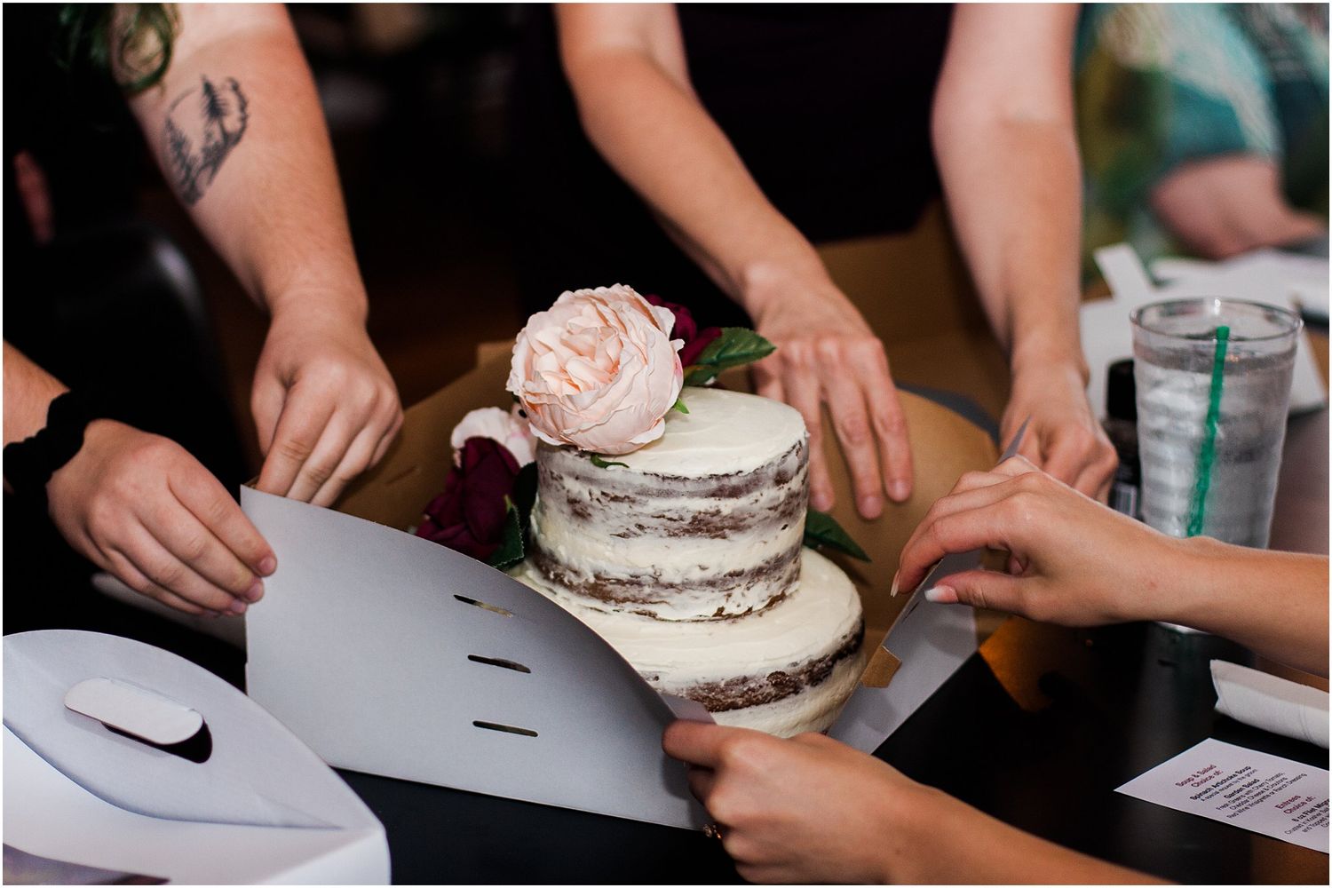 Hands decorating a rustic naked cake with blush pink roses on top.