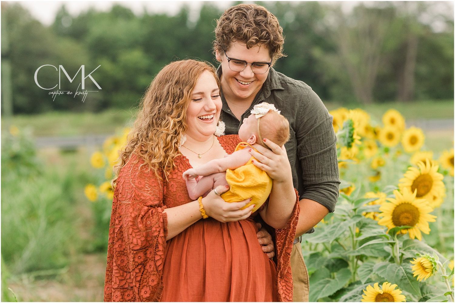 Loving family moment captured in sunflower field with baby wearing yellow outfit.