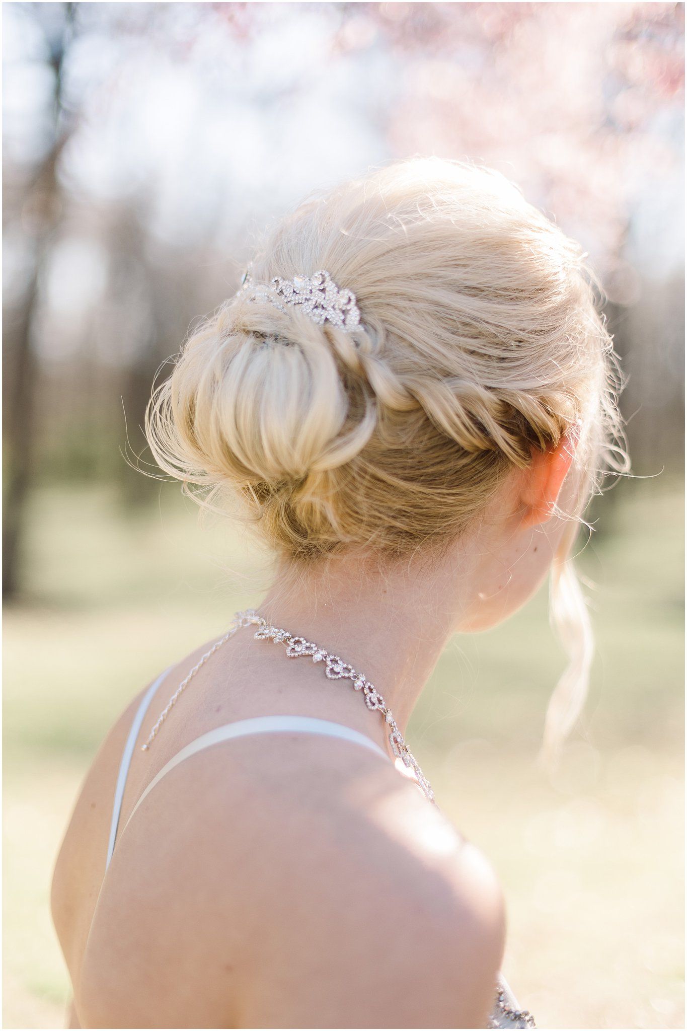 Elegant updo hairstyle with crystal hair accessory and necklace detail.