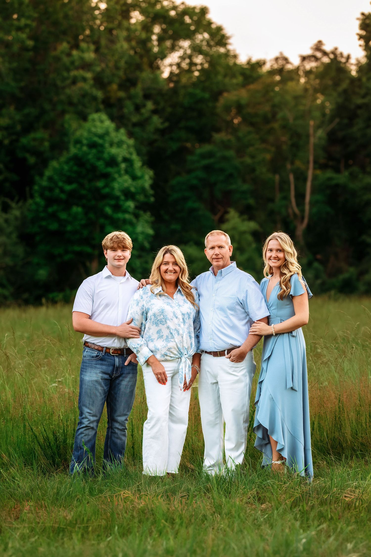 Family group photo in a grassy field at sunset wearing coordinated blue and white outfits.
