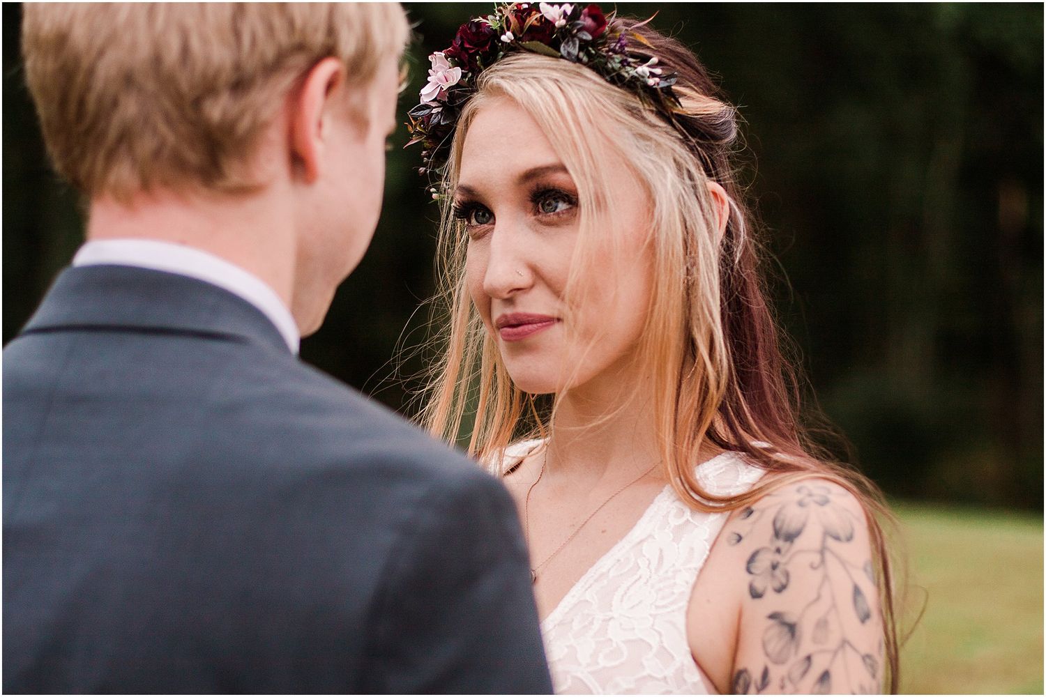 Intimate wedding moment captured showing a light-haired bride in a floral crown looking lovingly at her groom outdoors.