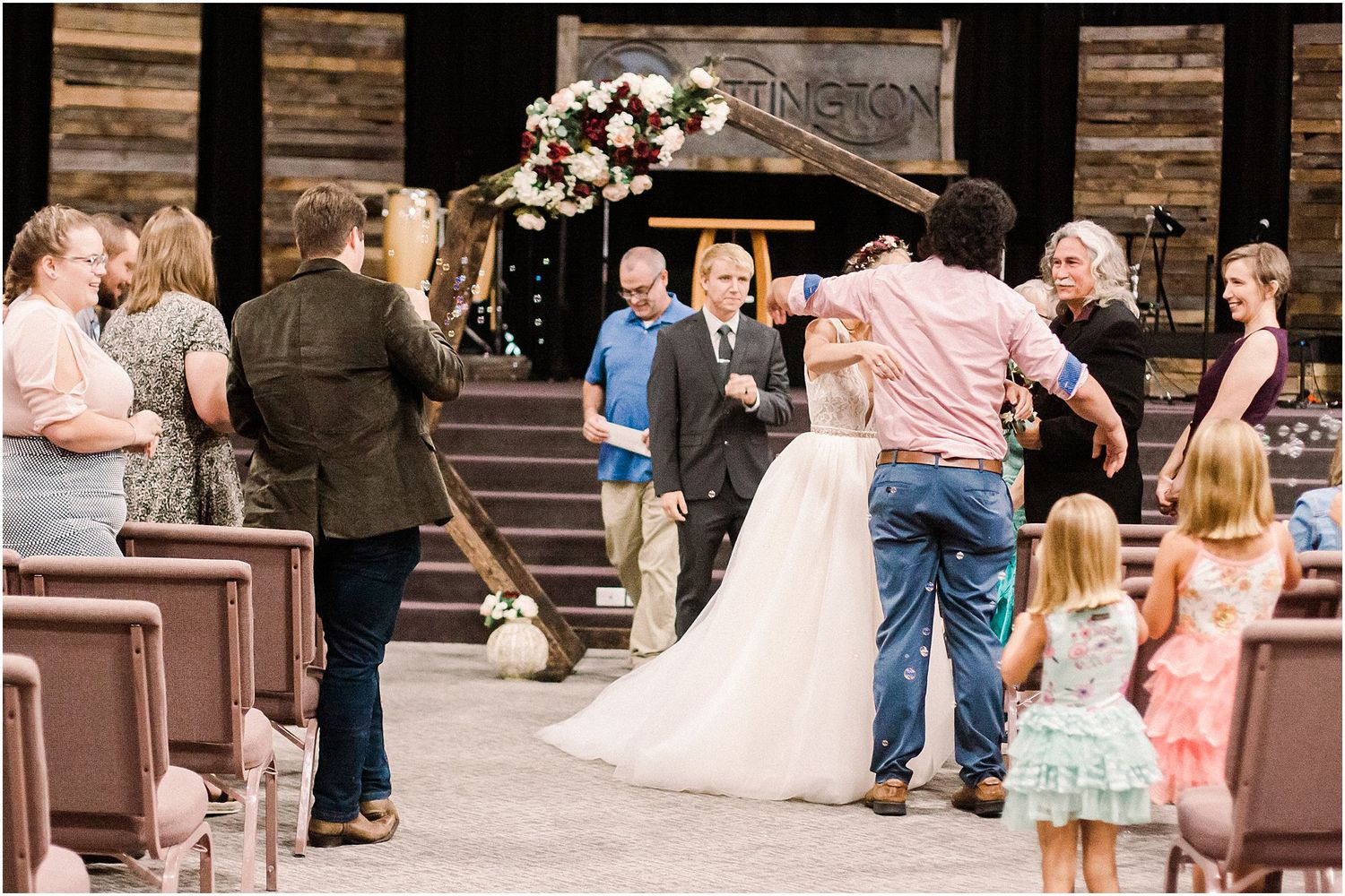 Wedding guests mingle and celebrate around the newlyweds under a rustic wooden arch.