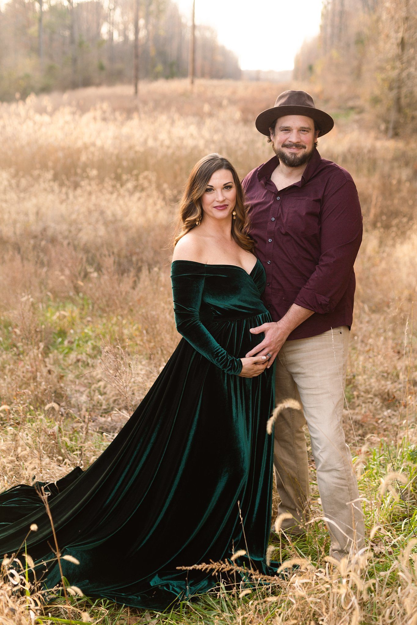 Romantic maternity portrait in field with emerald dress and casual menswear.