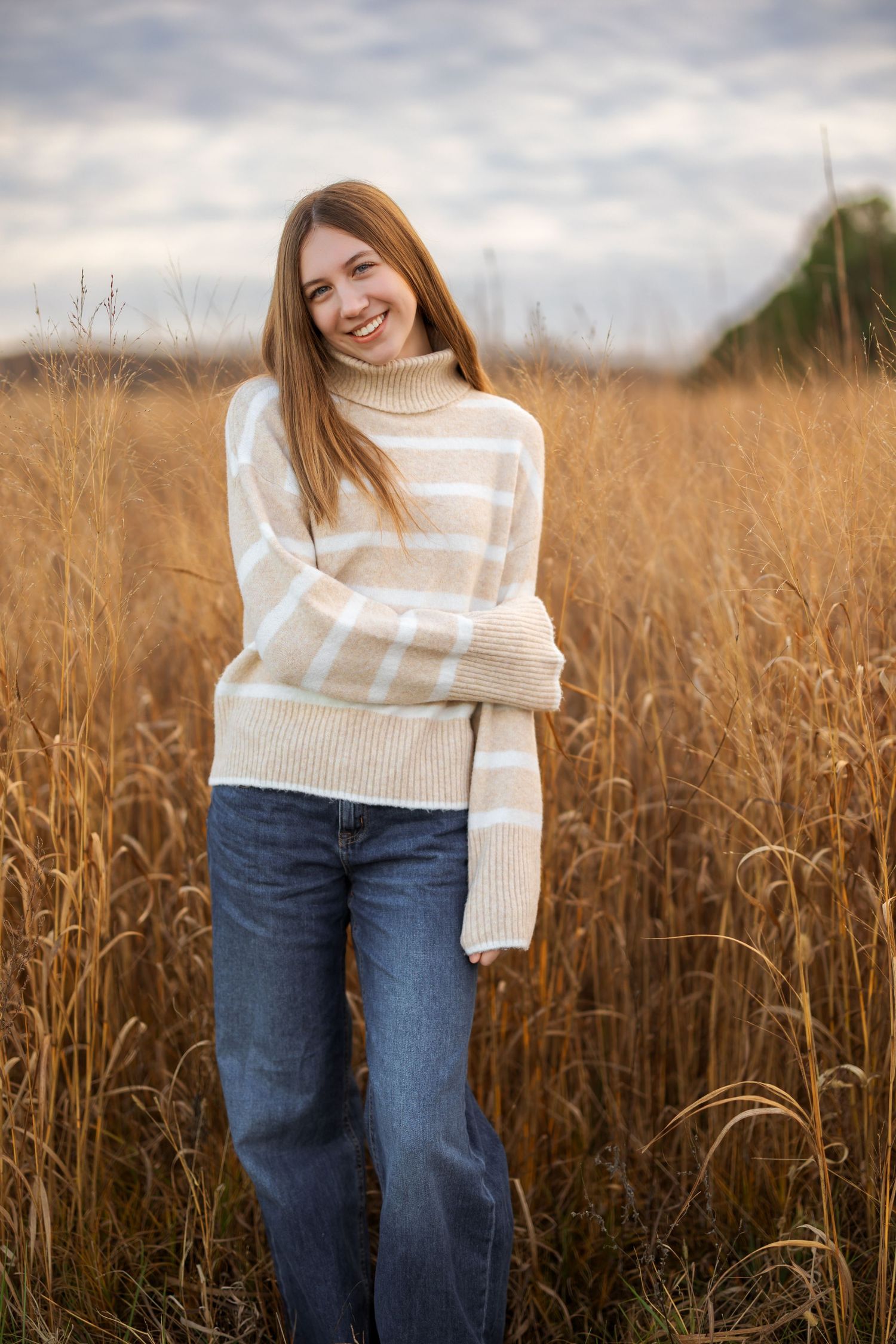 Person in cream striped sweater posing in golden wheat field at sunset.