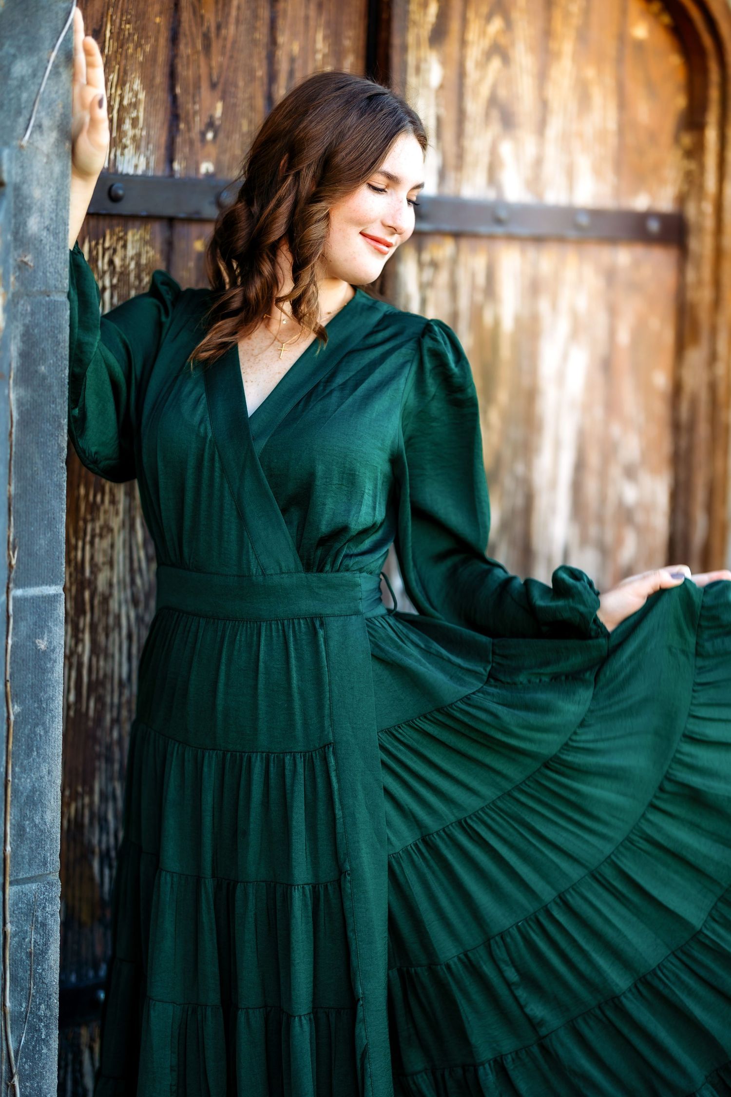 Elegant spinning poses in an emerald green dress against a rustic wooden backdrop.