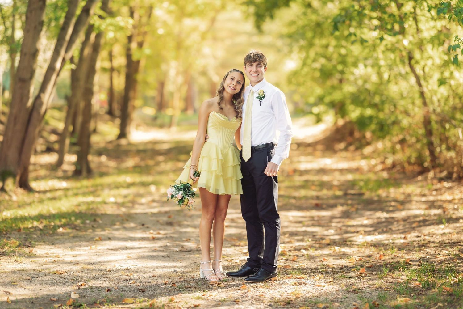 Couple posing together in a sunlit wooded area during an outdoor photo session.