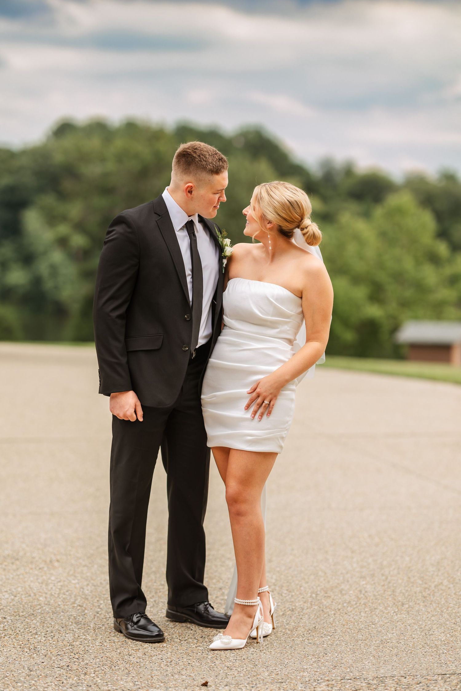 Wedding couple in formal attire posing together on an outdoor paved surface.