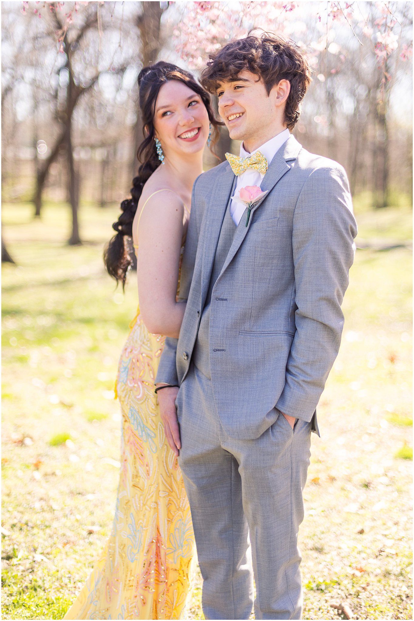 Couple laughing together in formal attire against spring blossom background.