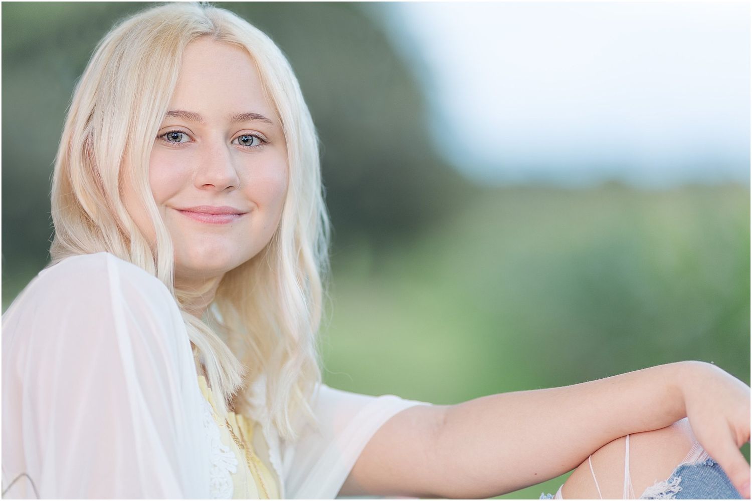 Senior girl leaning against a tree by a corn field