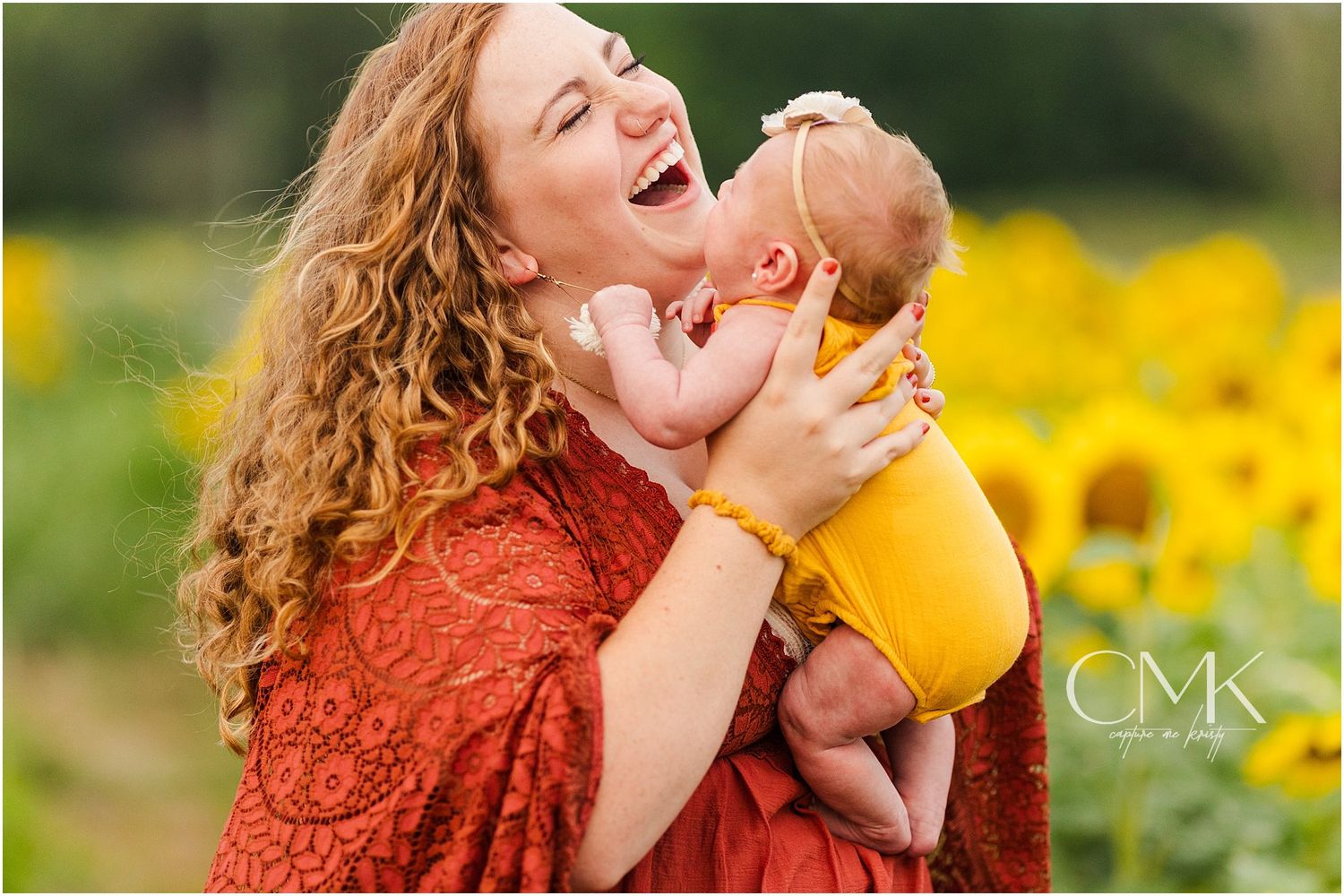 Candid moment of laughter while holding infant in yellow against sunflower backdrop.