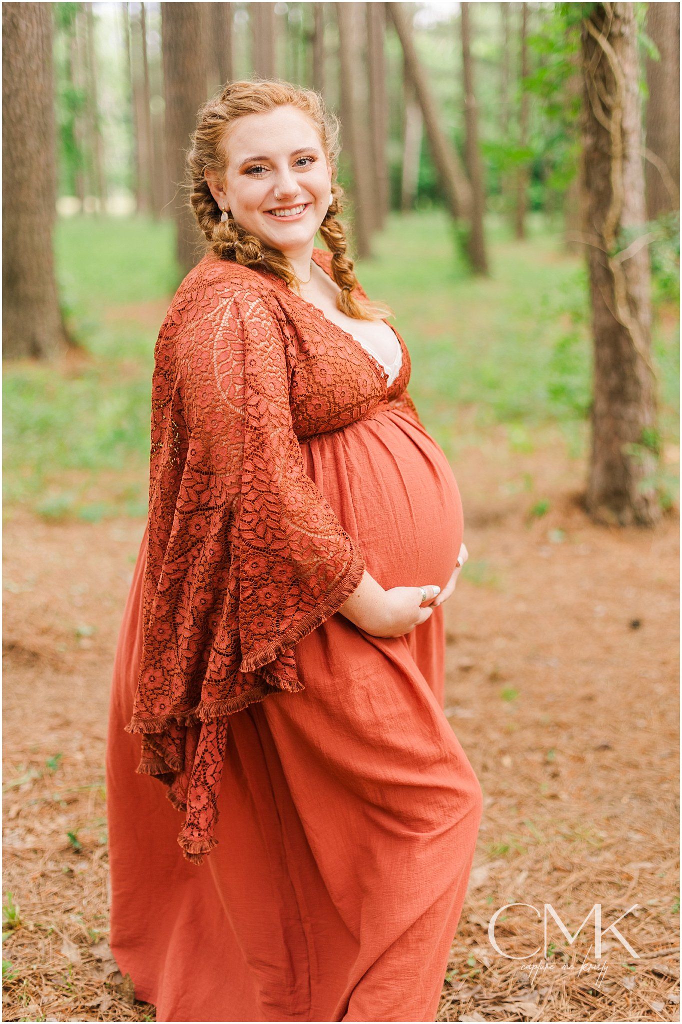 Maternity photo in a forest setting showing a rust-colored lace dress and flowing maxi dress.