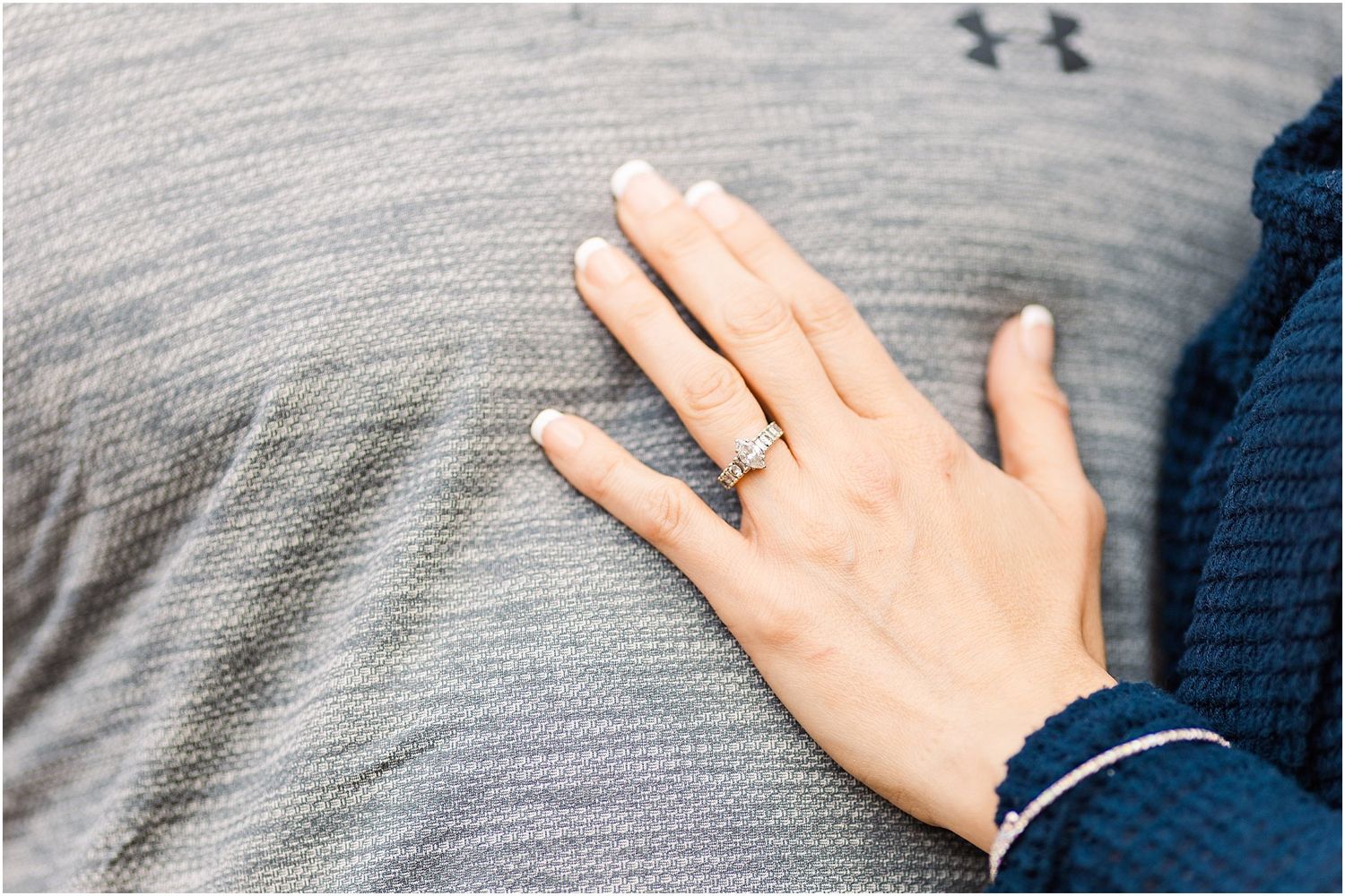 Close up of an engagement ring on a hand resting against a gray shirt.