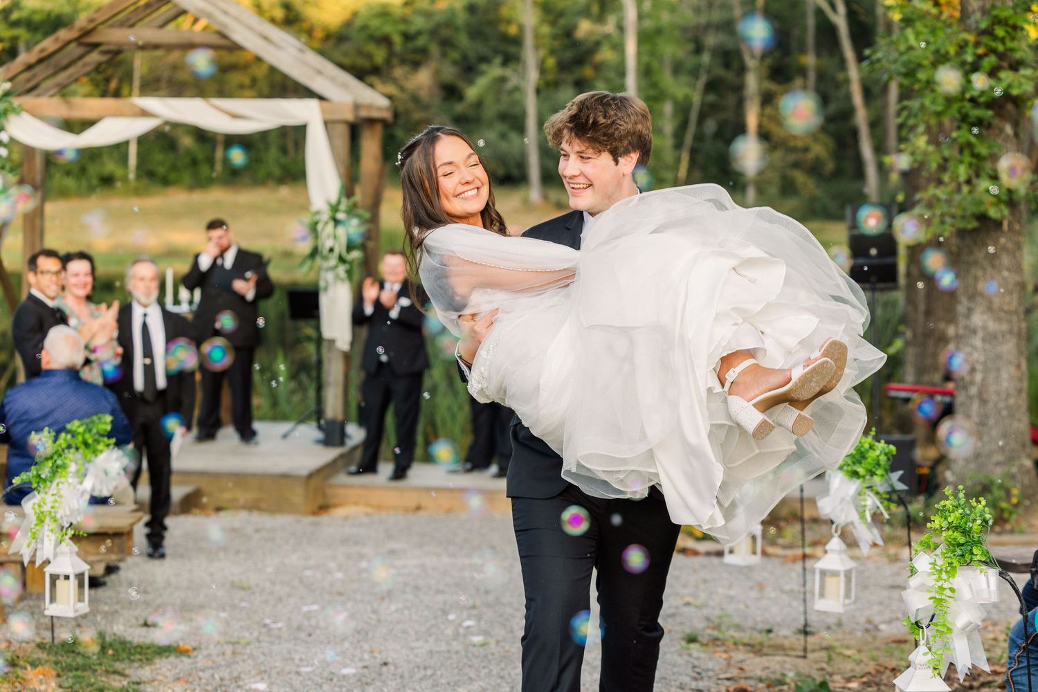 A celebratory moment with bubbles as the groom carries his bride during their outdoor wedding.