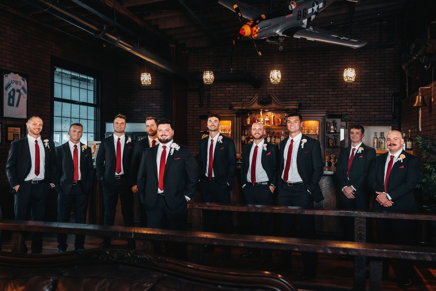 Wedding party members in formal attire gather in a dimly lit venue with brick walls.