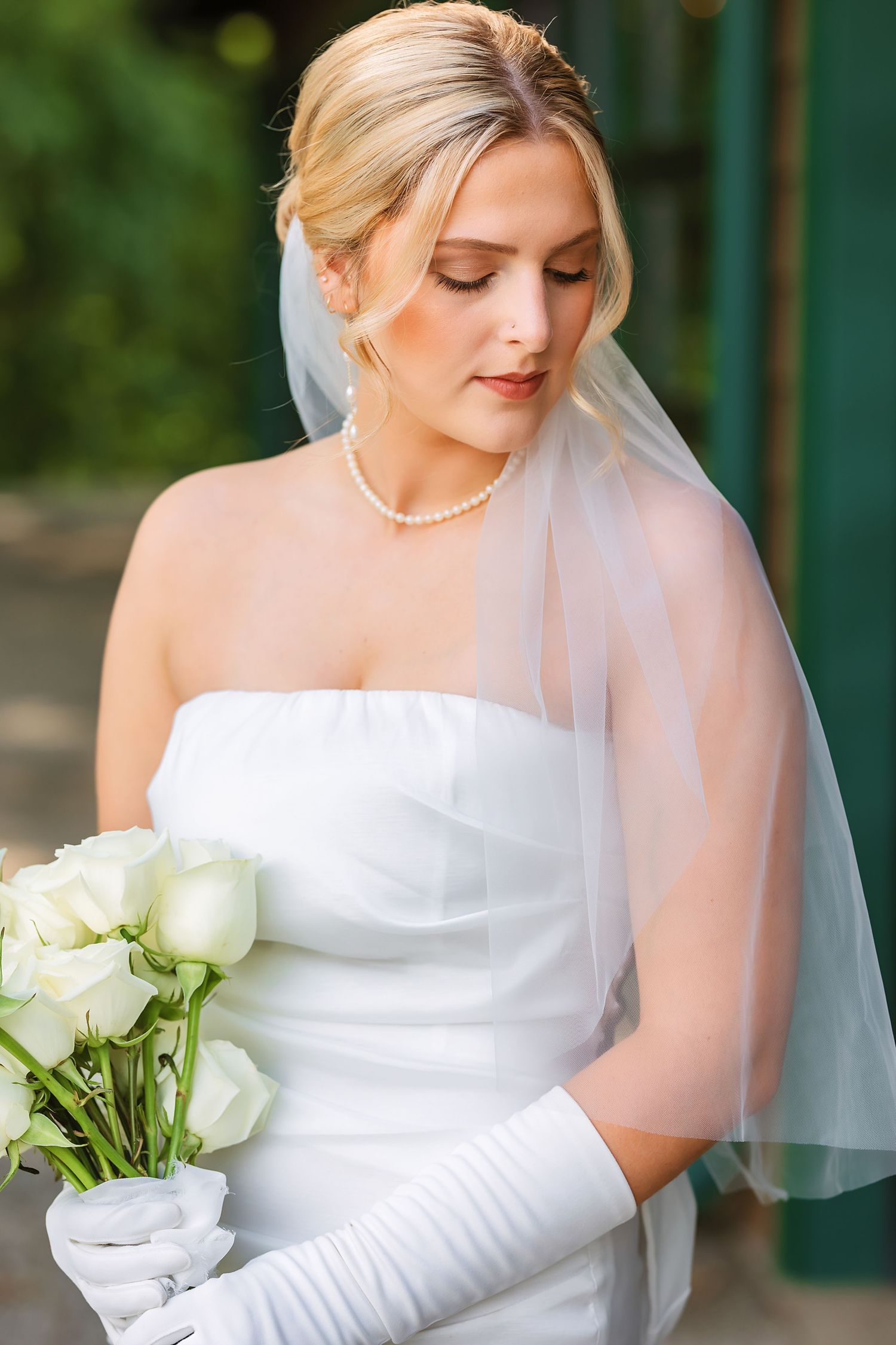 Close-up portrait of bride holding white roses and wearing pearl necklace.
