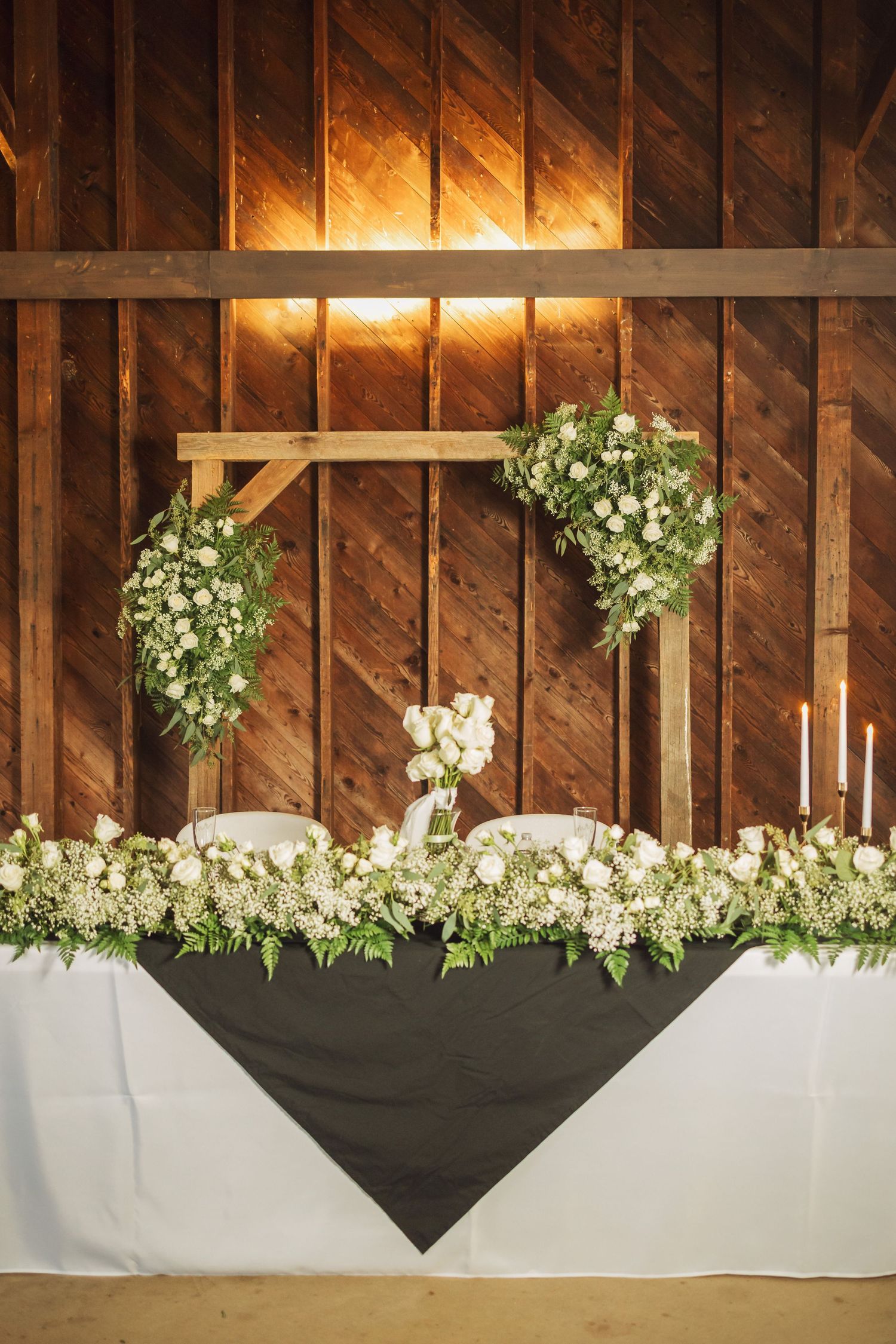 Rustic barn wall decorated with white floral arrangements and draped fabric for a wedding ceremony.