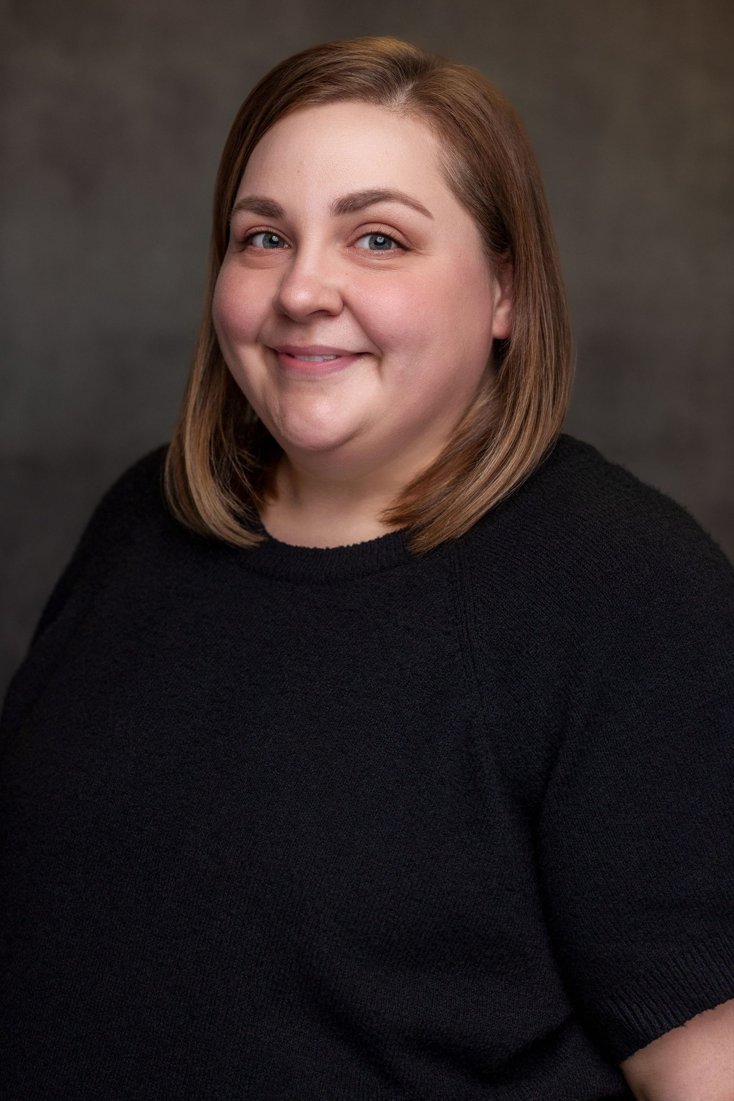 Studio portrait of woman in black sweater against neutral background.