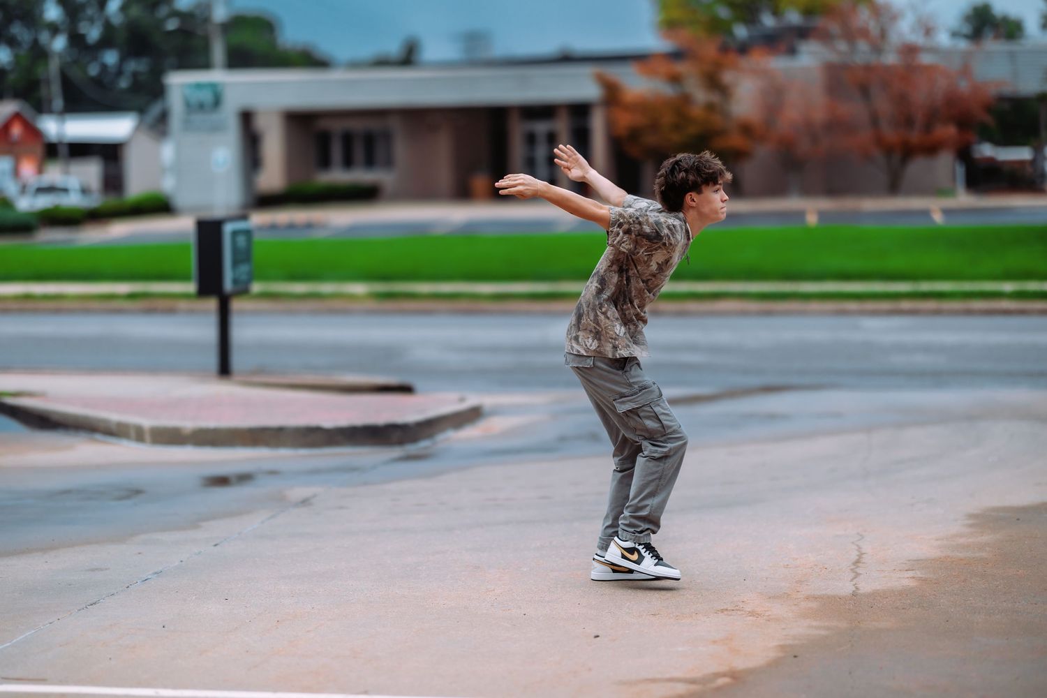 A skateboarder performs a trick at a skate park on a cloudy day with autumn trees in the background.