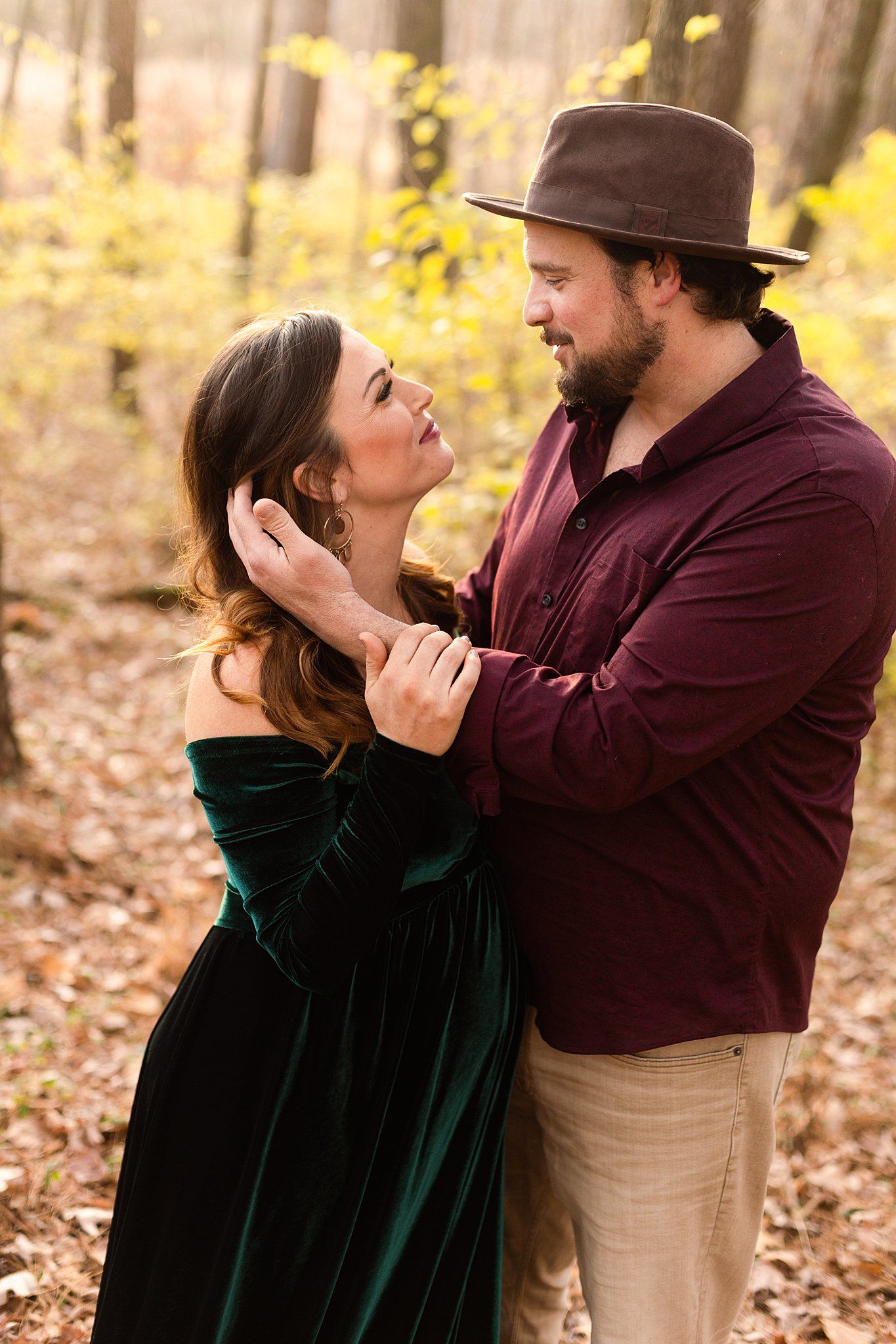 Intimate couple moment captured in fall forest with emerald dress and burgundy shirt.