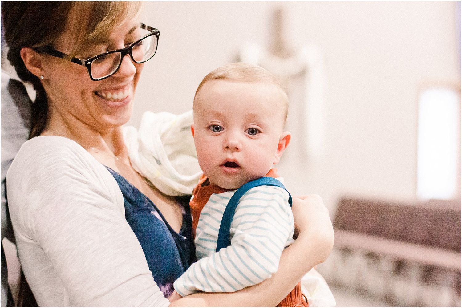Candid moment of a young infant in white clothing being held during an indoor event.