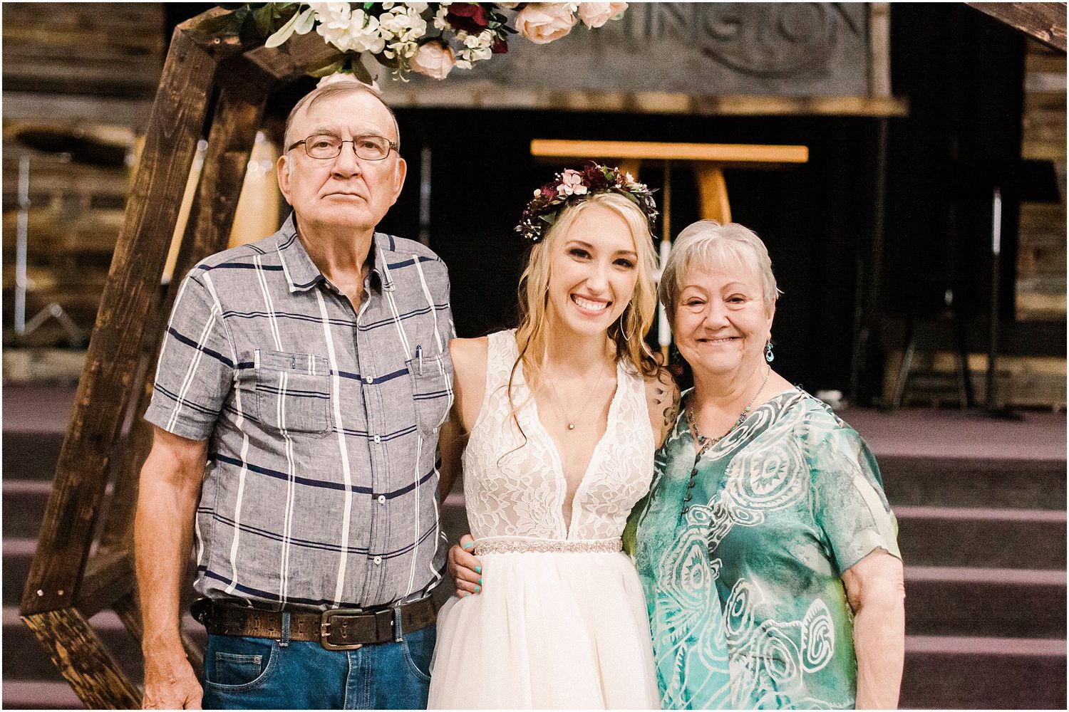 Wedding portrait with rustic wooden arch and floral decorations in background.