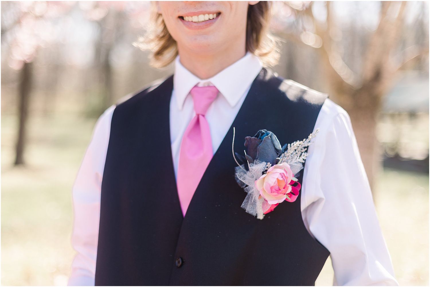 Formal attire detail showing pink tie and floral boutonniere against black vest.