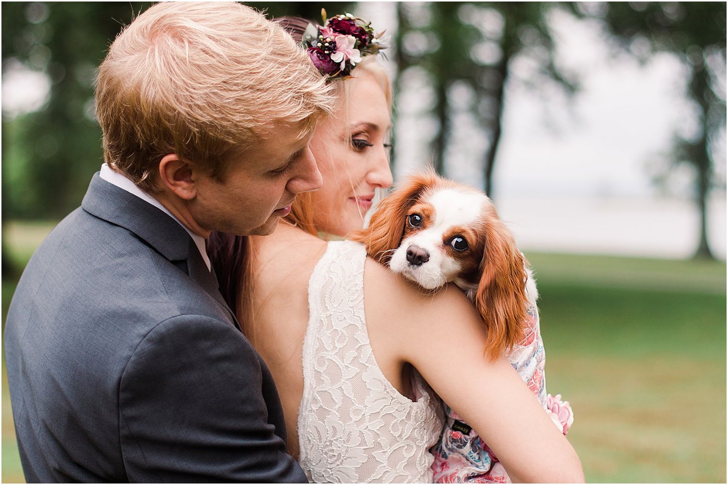 A couple embraces while holding their Cavalier King Charles Spaniel during their outdoor wedding photoshoot.