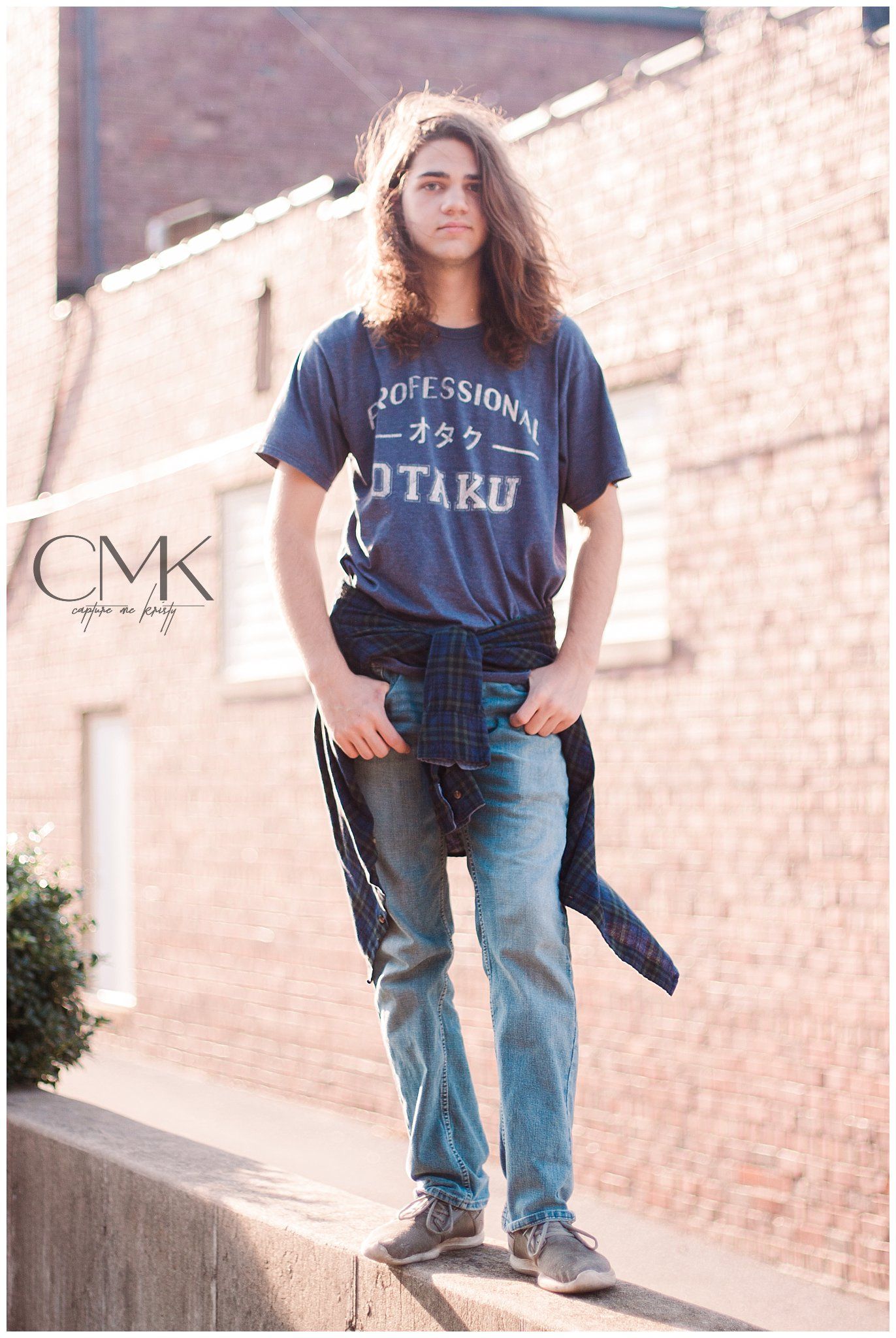 Person wearing navy otaku t-shirt and jeans standing against brick wall.
