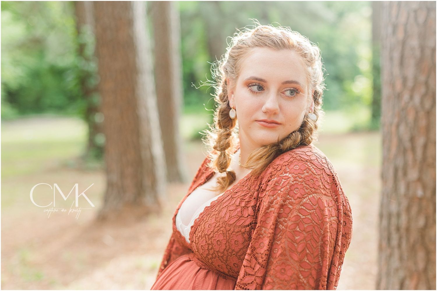 Maternity portrait featuring expectant mother in rust dress against forest backdrop.