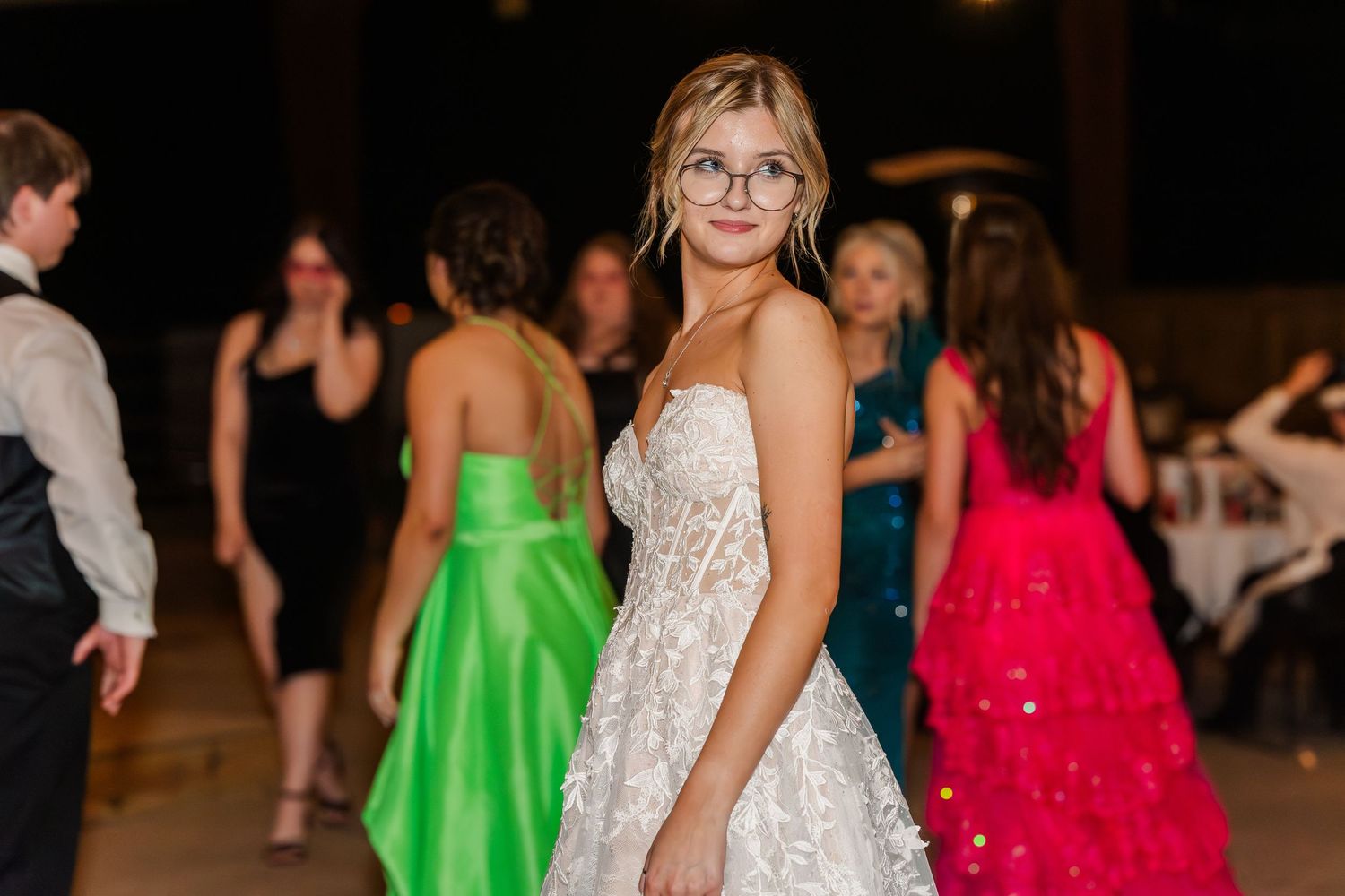 Attendees in colorful formal dresses including bright green and red gather at an evening event.